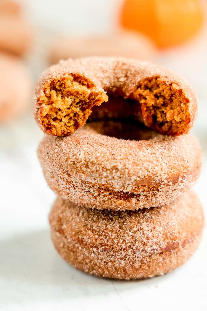 three pumpkin donuts stacked with a bite out