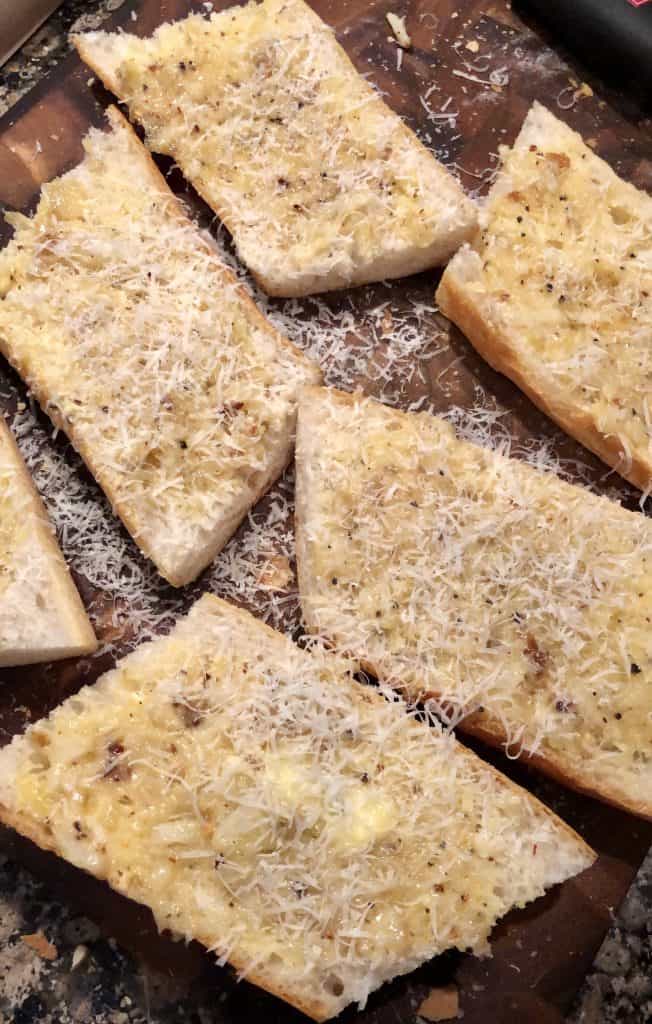 garlic butter spread over french bread with fresh parmesan over the top