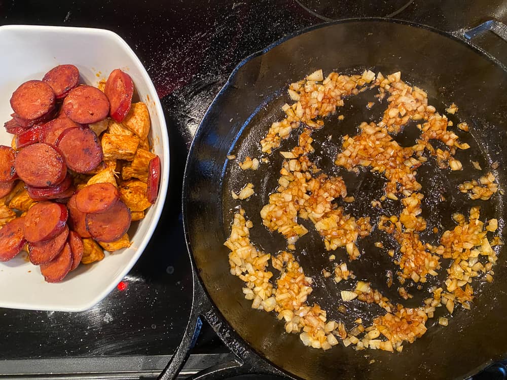 photo of stove top with cast iron skillet and onions inside, and bowl with chorizo and chicken