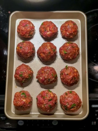 over head shot of meatballs rolled into balls on a baking pan