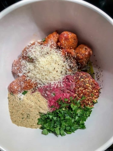 over head shot of white bowl with hot italian sausage, beef, red pepper flakes, basil, bread crumbs, and parmesan.