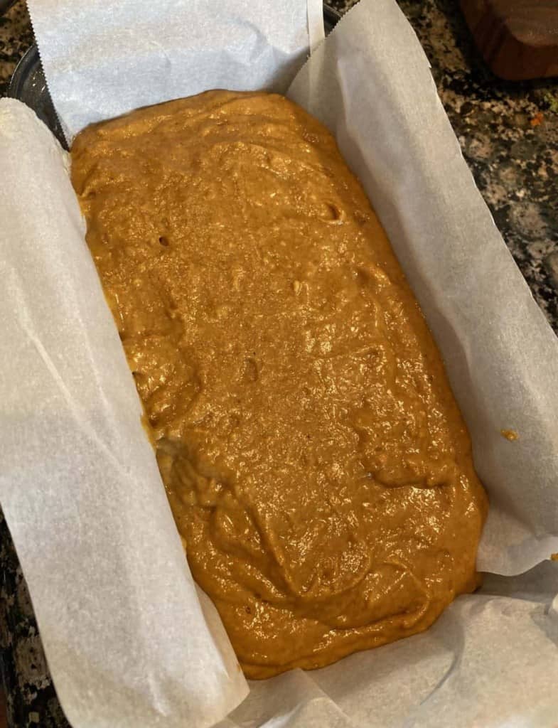 pumpkin bread batter in a loaf pan with parchment paper around it