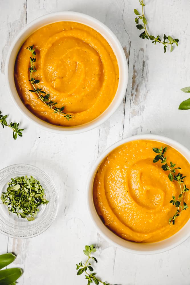 two white bowls with butternut squash soup surrounded by fresh thyme and sage