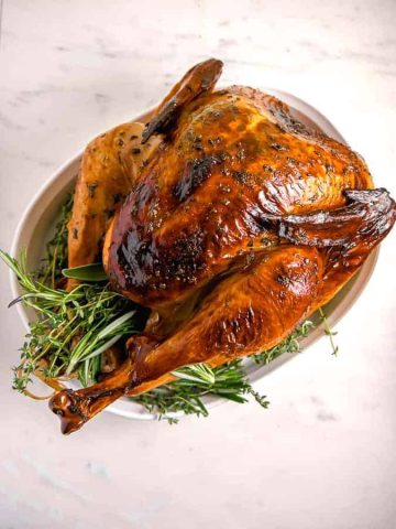 overhead photo of a roasted turkey with crispy brown skin and herbs surrounding