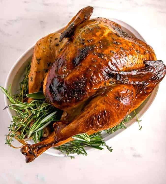 overhead photo of a roasted turkey with crispy brown skin and herbs surrounding