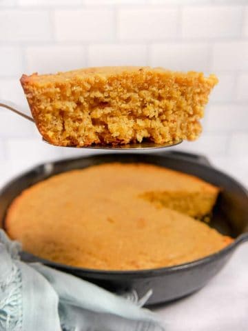 slice of cornbread on a serving spoon with cast iron in background