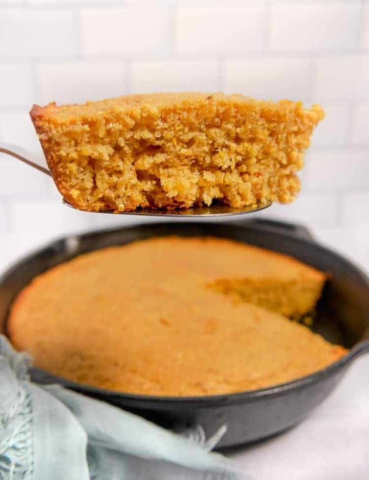 slice of cornbread on a serving spoon with cast iron in background