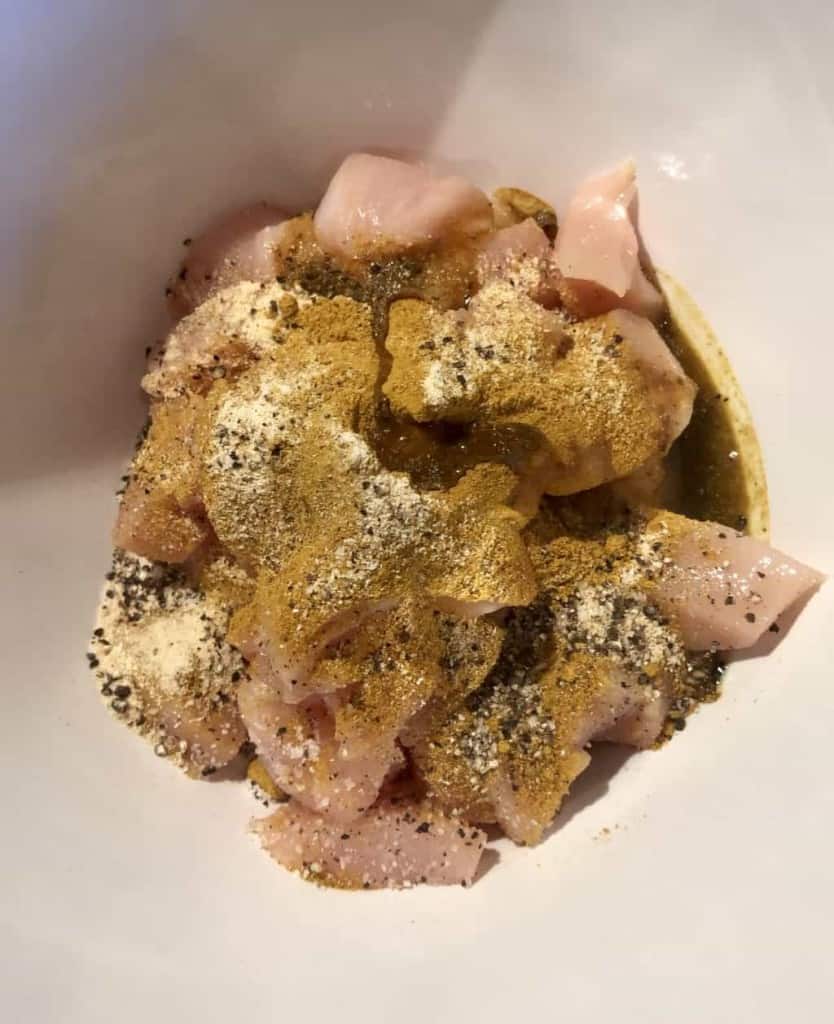 chicken curry spices over cubed chicken in a bowl