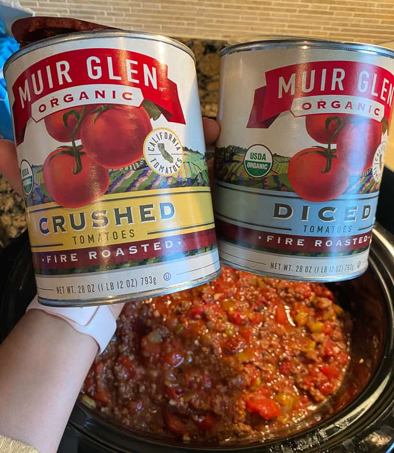 holding two cans of fire roasted tomato cans over chili