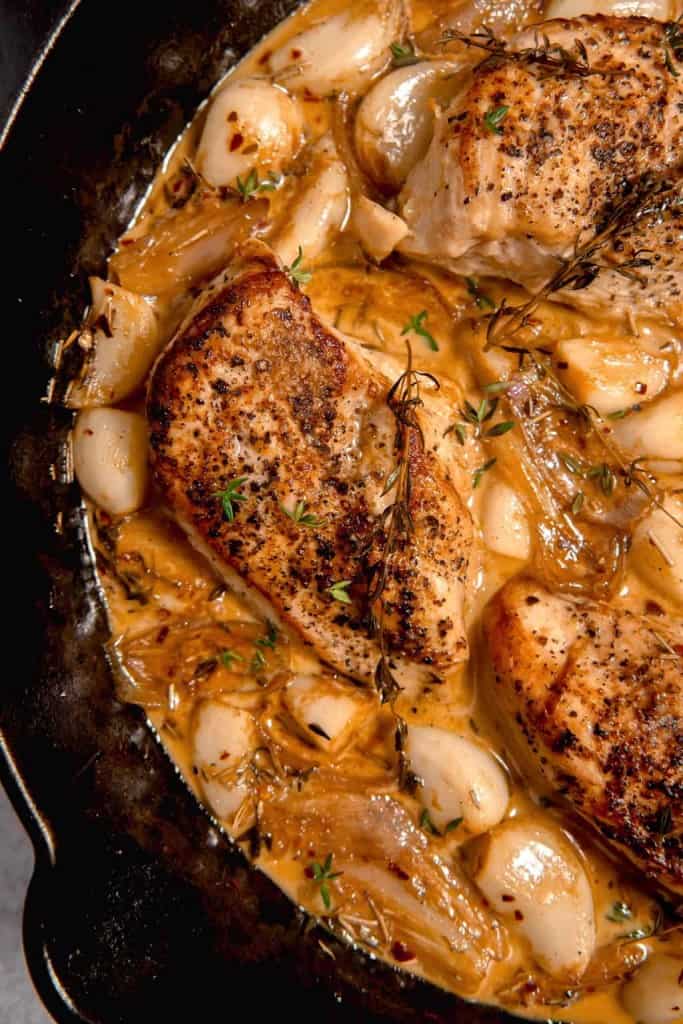 close up overhead picture of a cast iron skillet with chicken surrounded by garlic and a white wine sauce