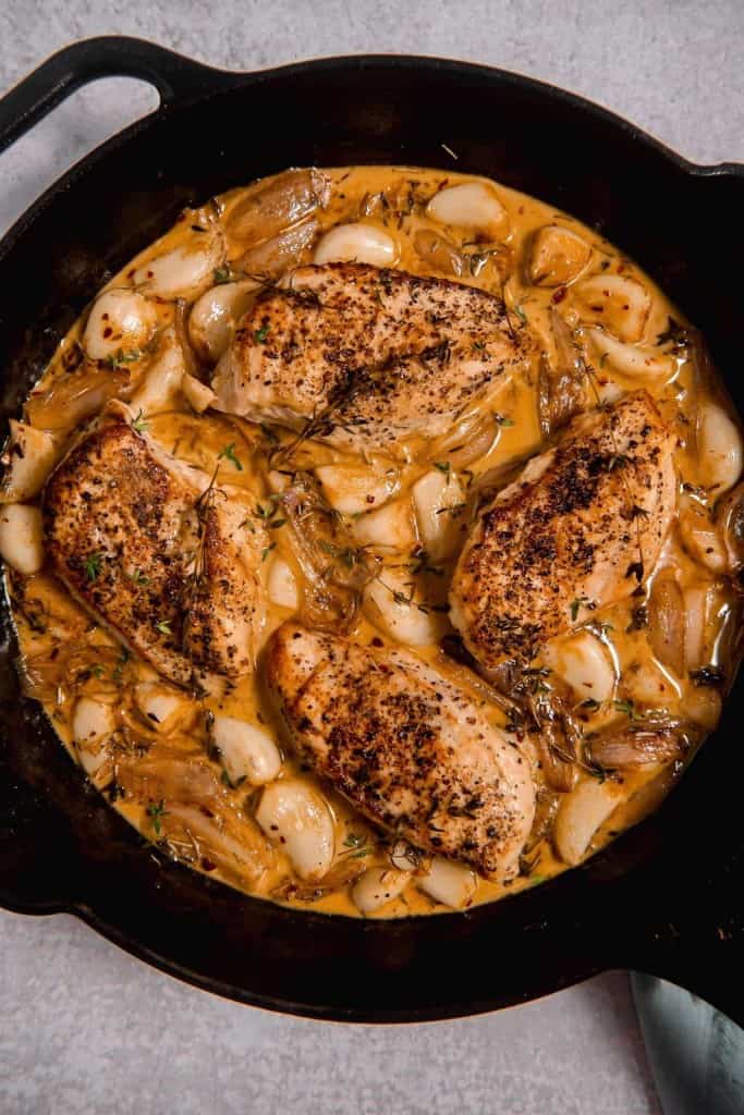 overhead picture of a cast iron skillet with chicken surrounded by garlic and a white wine sauce