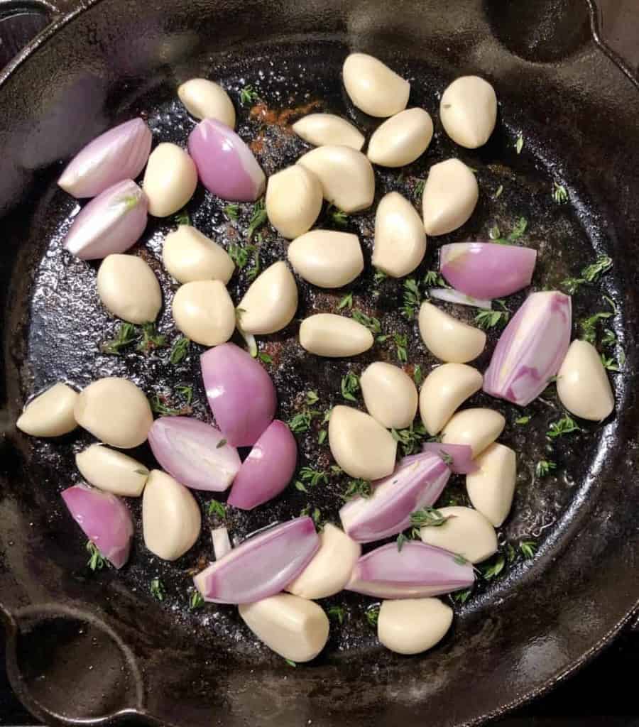 garlic cloves and shallots in a cast iron skillet