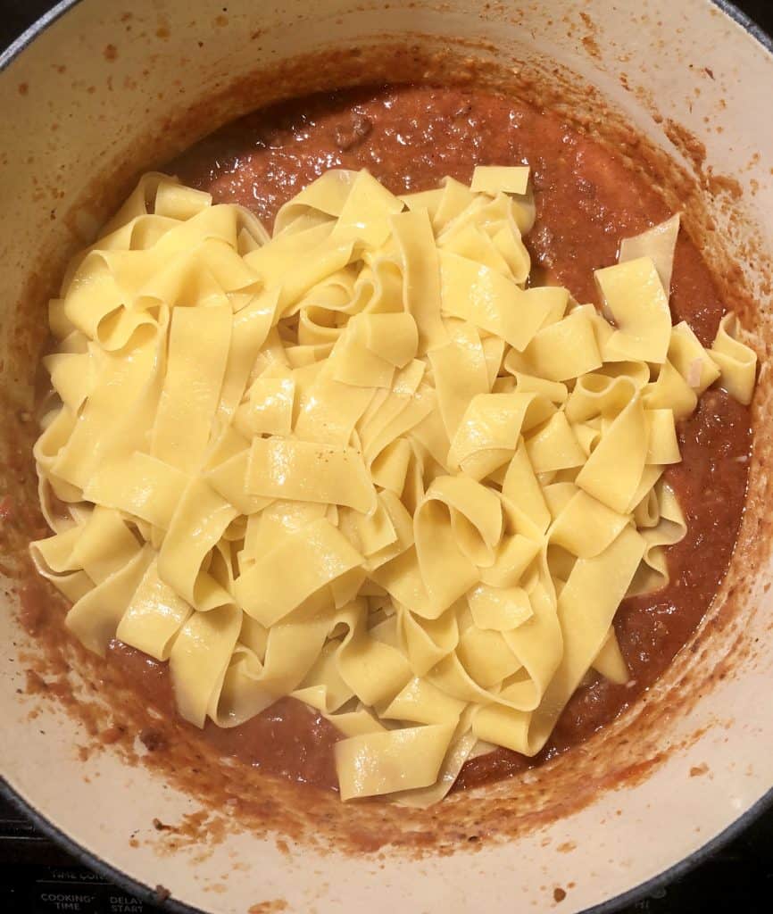 pappardelle over the top of bolognese sauce in a dutch oven