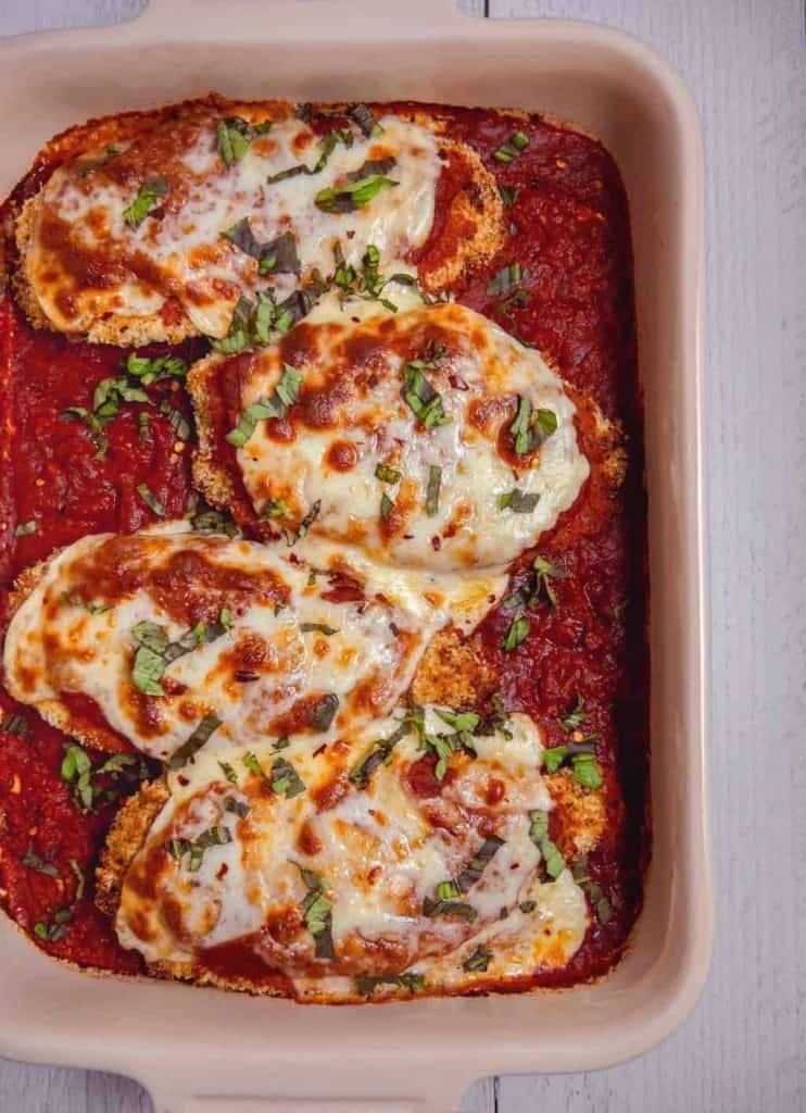 Overhead baked chicken parmesan in baking dish with red sauce fresh basil and bubbly creese