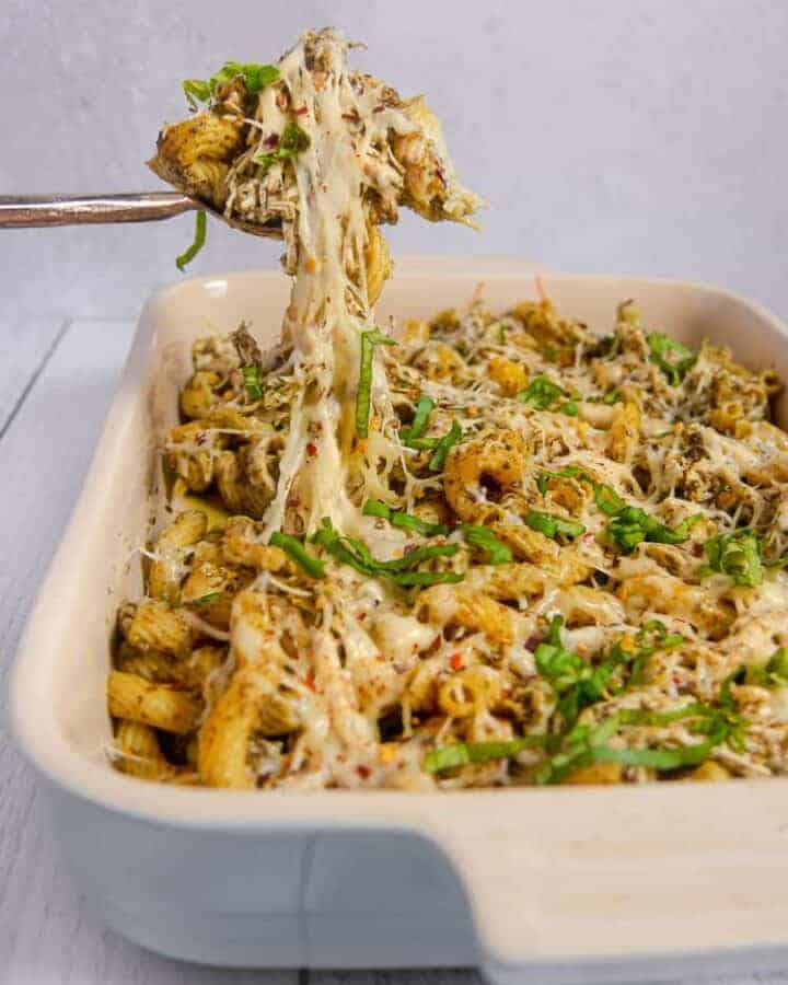 rectangular baking dish with pesto pasta and melty cheese being lifted out of the dish with a spoon