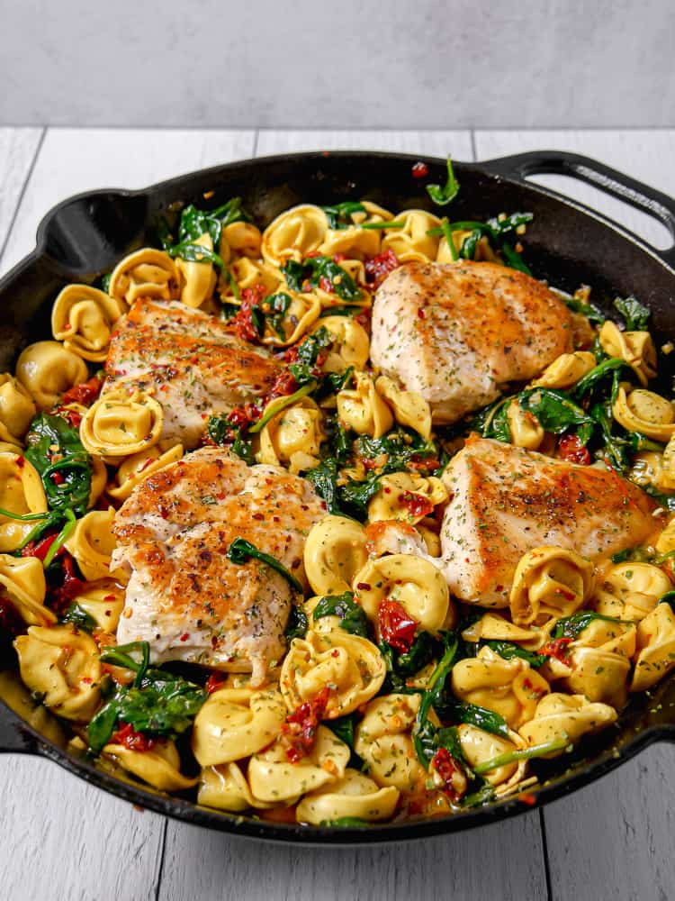 cast iron skillet with cheese tortellini, spinach, tomatoes, and seared chicken breast