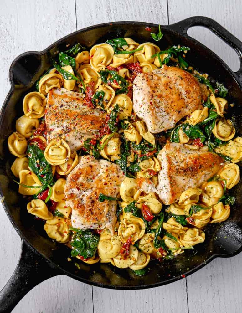 cast iron skillet with cheese tortellini, spinach, tomatoes, and seared chicken breast