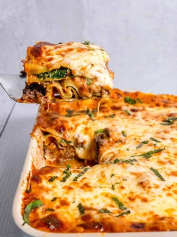 spinach and cheese lasagna being lifted out of rectangular baking dish