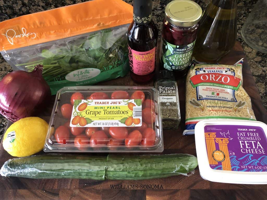 cutting board with all ingredients of orzo pasta salad shown