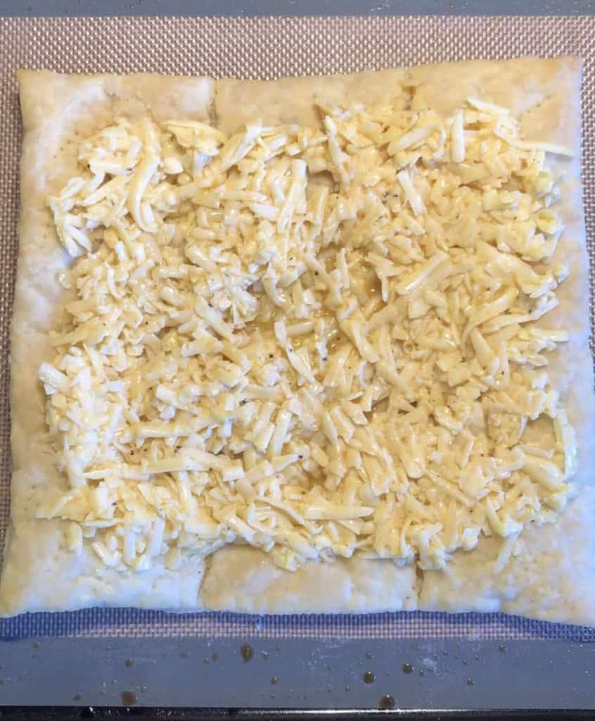overhead shot of cheese mixture spread over the puff pastry on a baking sheet