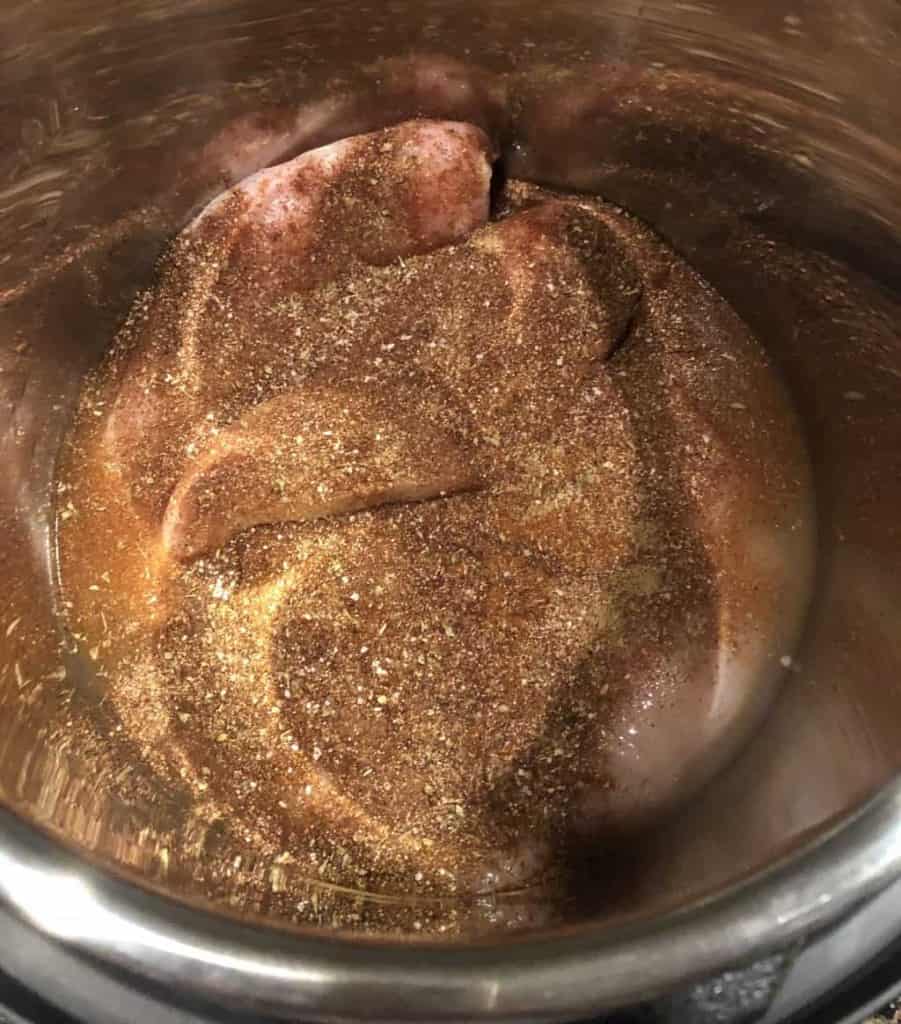 overhead shot of uncooked chicken breast in the instant pot pressure cooker with spices spread over the top