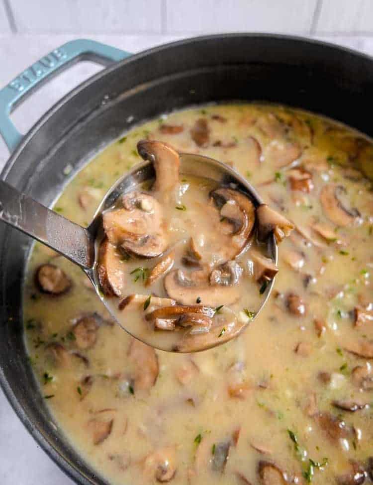 soup pot filled with mushroom soup and herbs with a ladle lifting soup out of pot