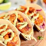 3 tacos with shrimp and drizzled avocado crema sauce on top