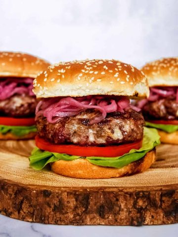 blue cheese burger with pickled red onion, lettuce, tomato, sesame seed buns, stacked on wood block