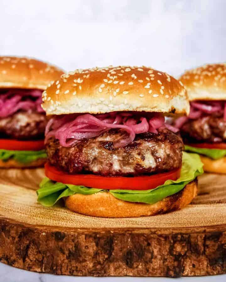 blue cheese burger with pickled red onion, lettuce, tomato, sesame seed buns, stacked on wood block