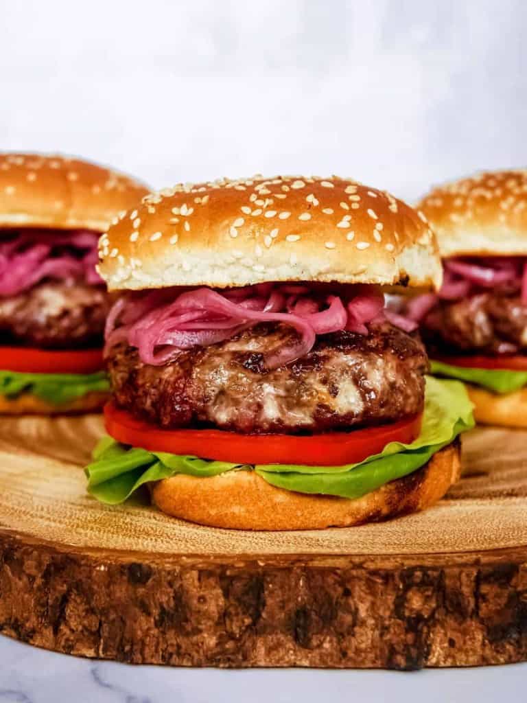 front close up shot of blue cheese burger with pickled red onion, lettuce, tomato, sesame seed buns, stacked on wood block
