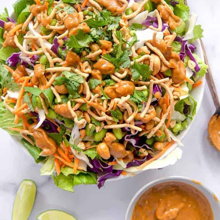 overhead photo of asian salad in a bowl with spicy peanut dressing on the side and sliced limes