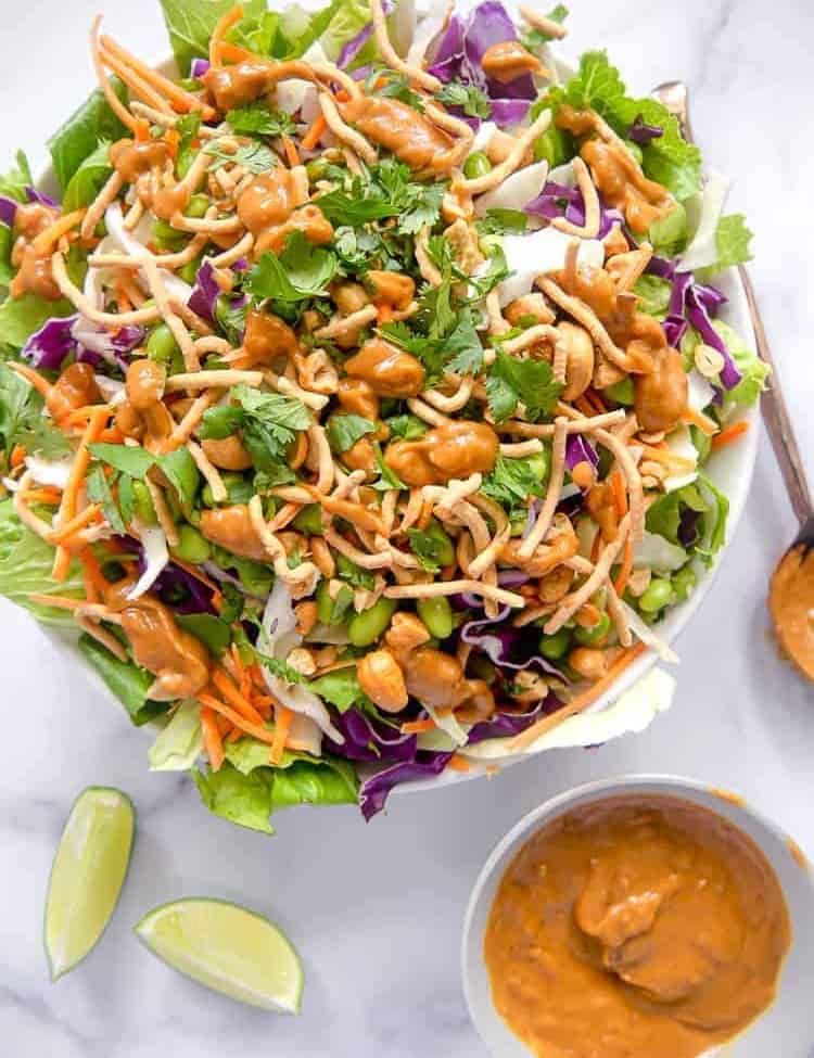 overhead photo of asian salad in a bowl with spicy peanut dressing on the side and sliced limes