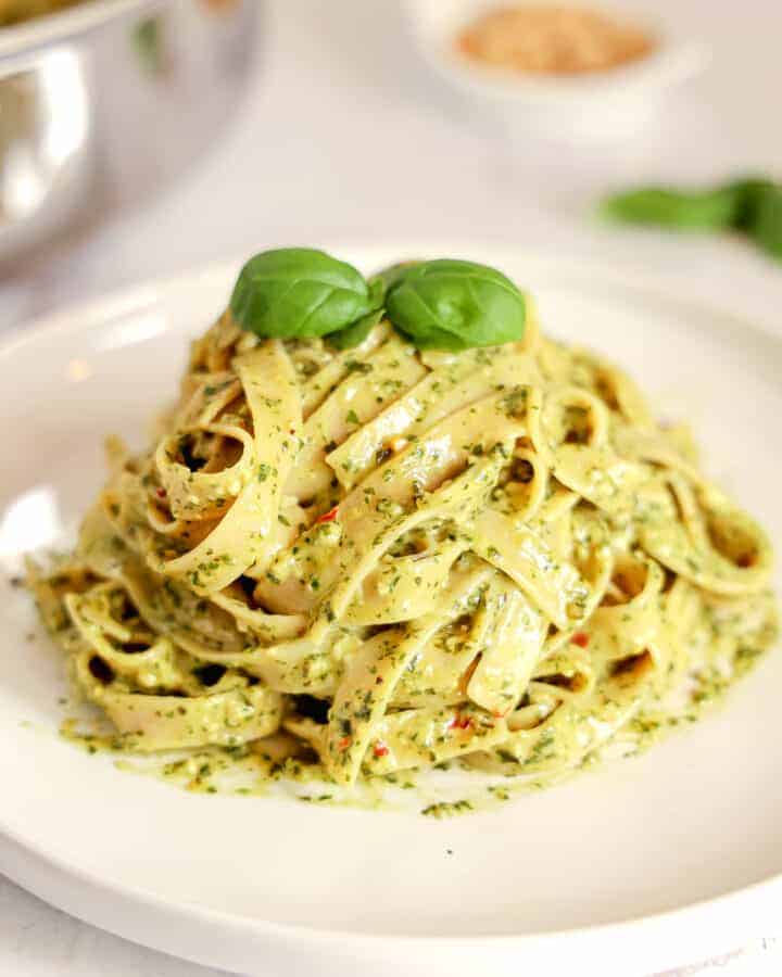 pile of pesto pasta on a white plate with a basil leaf on top