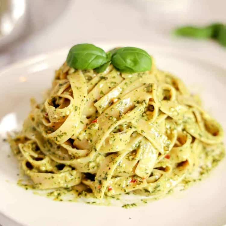 pile of pesto pasta on a white plate with a basil leaf on top