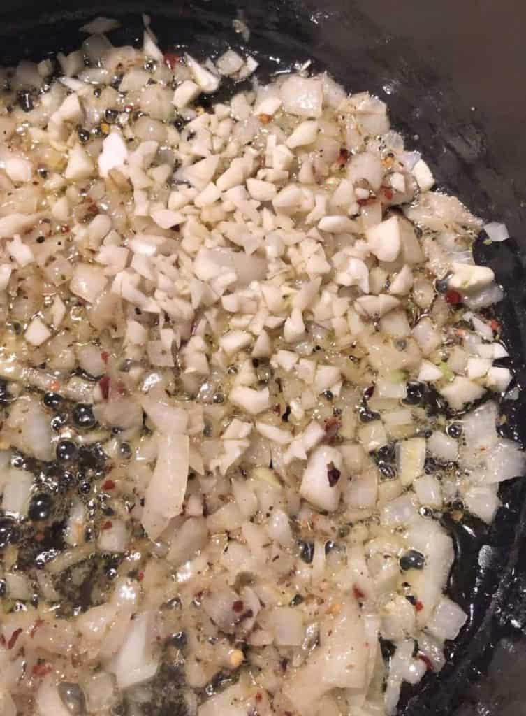 close up of diced onion, garlic, and red pepper flakes being sautéed in a dutch oven 