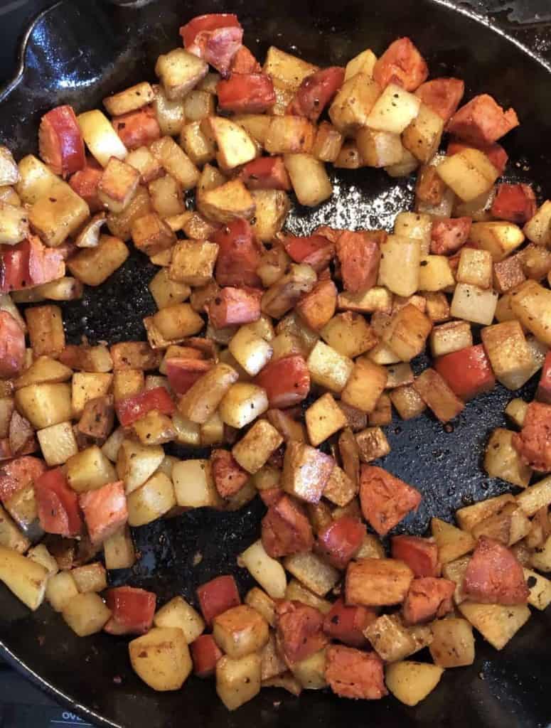 diced potatoes and chorizo in a cast iron skillet with four empty wells created