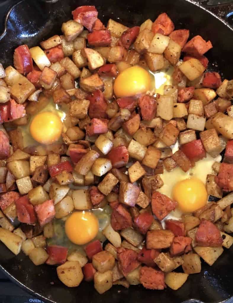 diced potatoes and chorizo in a cast iron skillet with four uncooked eggs cracked on top