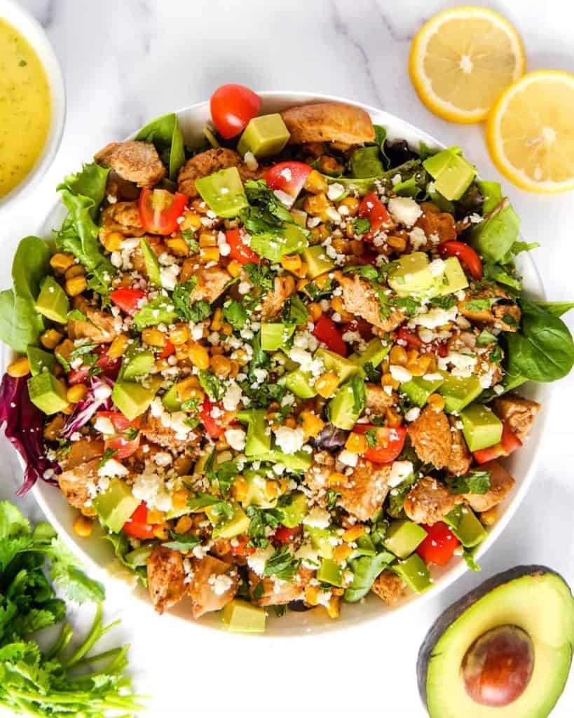 overhead shot of the Mexican garden chicken salad with lettuce, chicken, avocado, corn, tomatoes, in a white bowl with cotija cheese over the top