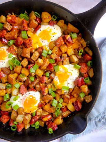 Close up of cast iron skillet with chorizo, diced potatoes, baked eggs, and cheese with green onion garnish
