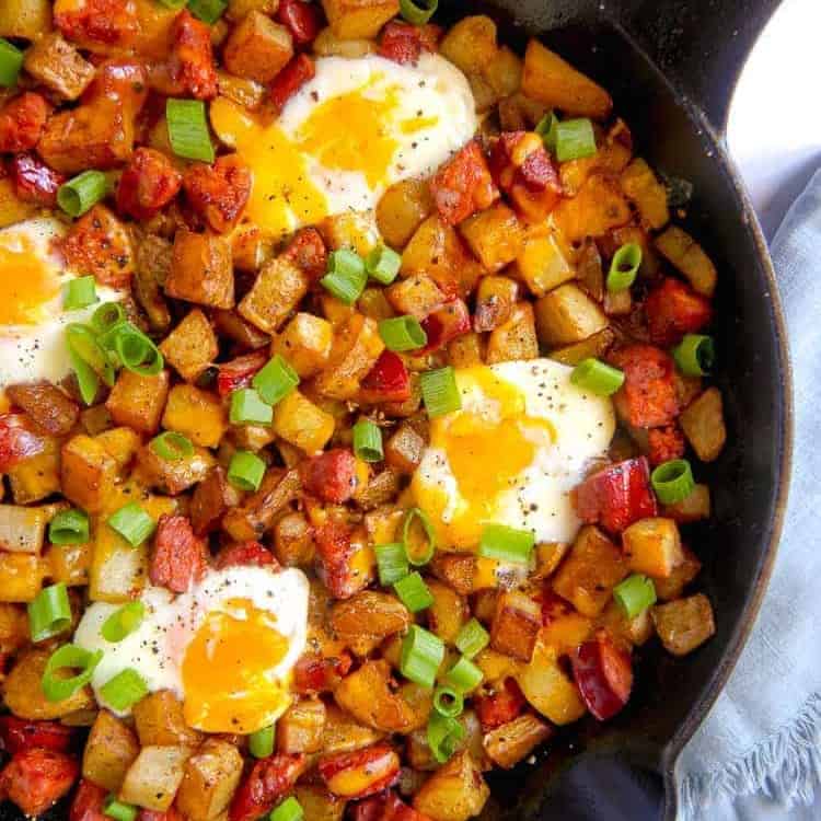 Close up of cast iron skillet with chorizo, diced potatoes, baked eggs, and cheese with green onion garnish