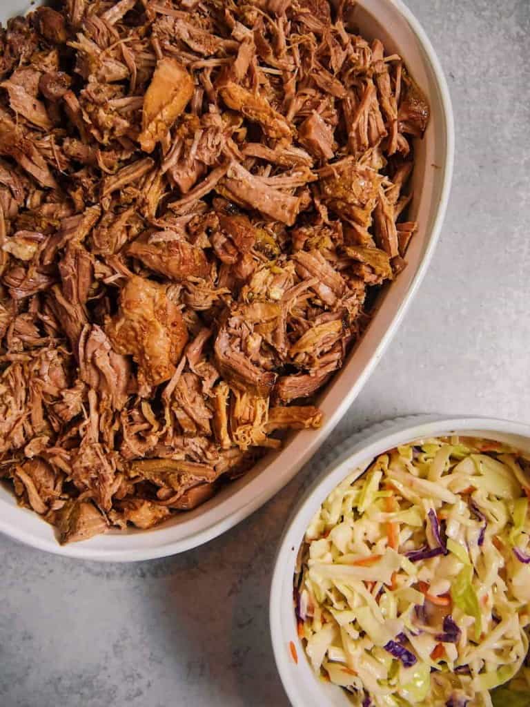 overhead shot of a white baking dish filled with pulled pork and a separate white bowl filled with coleslaw side by side