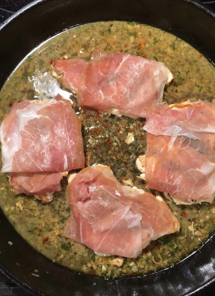 cast iron skillet with chicken breasts and fresh prosciutto on top