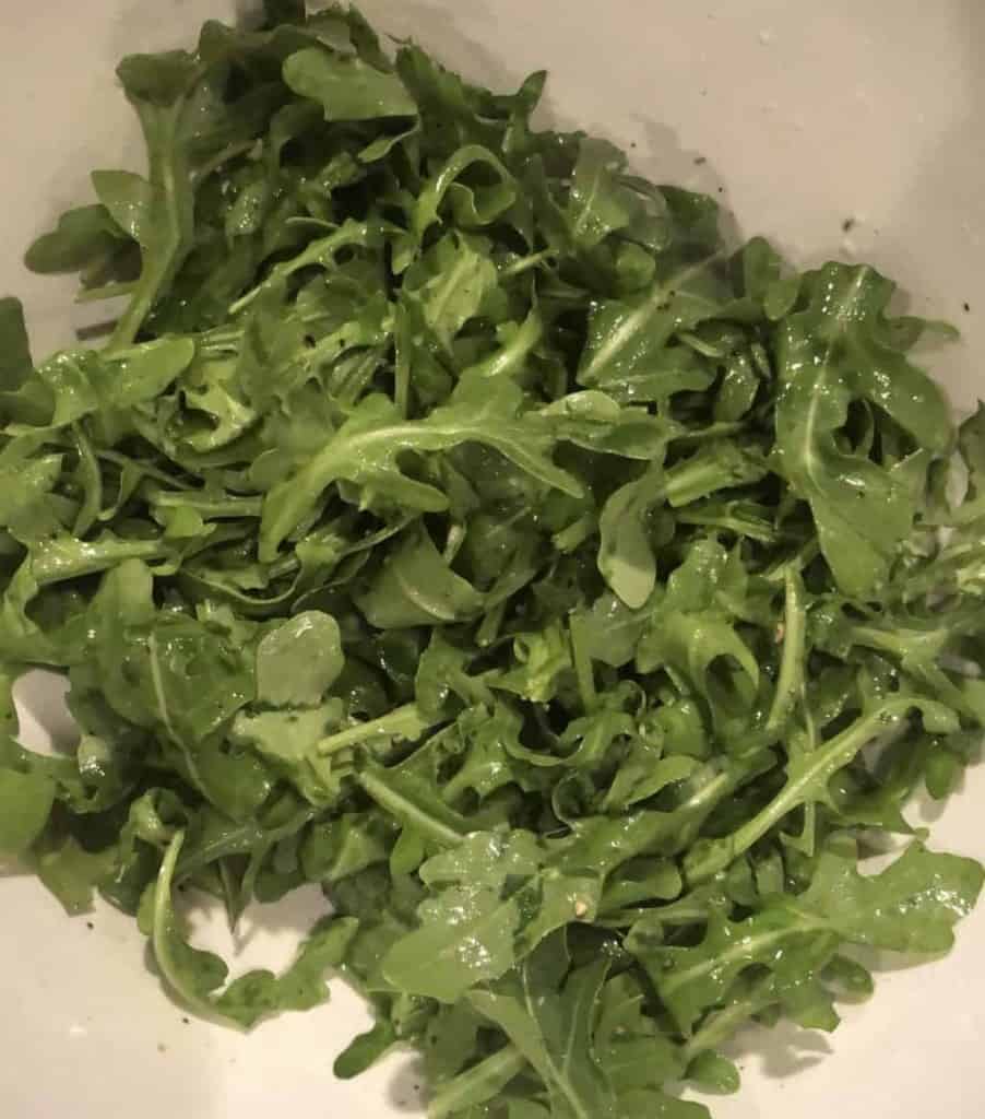 arugula in a bowl tossed in olive oil and lemon juice