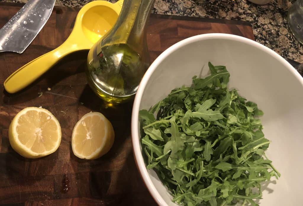 bowl of arugula, 2 lemon halves, a citrus squeeze, and olive oil