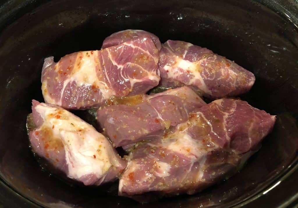 overhead shot of uncooked pork shoulder pieces in a crockpot with italian dressing drizzled over the top