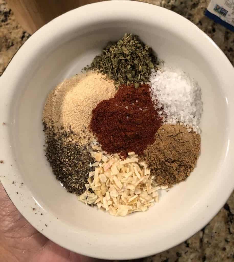 overhead shot of a dish with spices of oregano, garlic powder, onion, black pepper, ground cumin, and salt