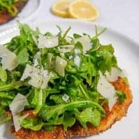 close up photo of chicken cutlet with arugula salad on top on a white plate