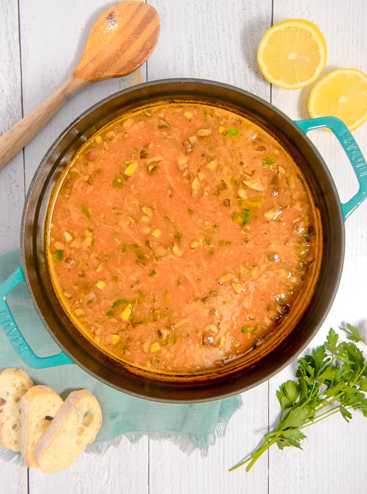 overhead photo of soup pot with vegetable orzo soup surrounded by bread, lemons, parsley and spoon