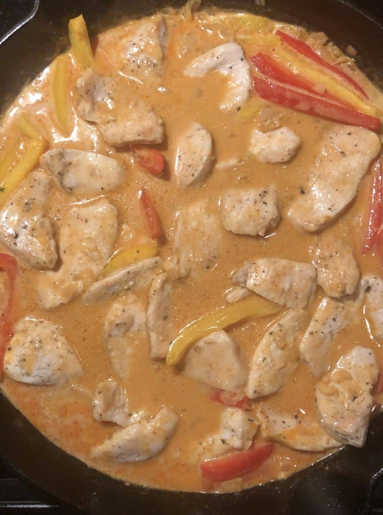 cast iron skillet with red coconut curry chicken broth and pieces of chicken and red bell peppers