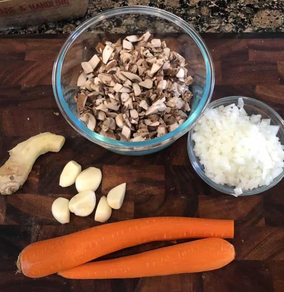 two carrots, 6 cloves garlic, knob of ginger, mushrooms, and onion on cutting board